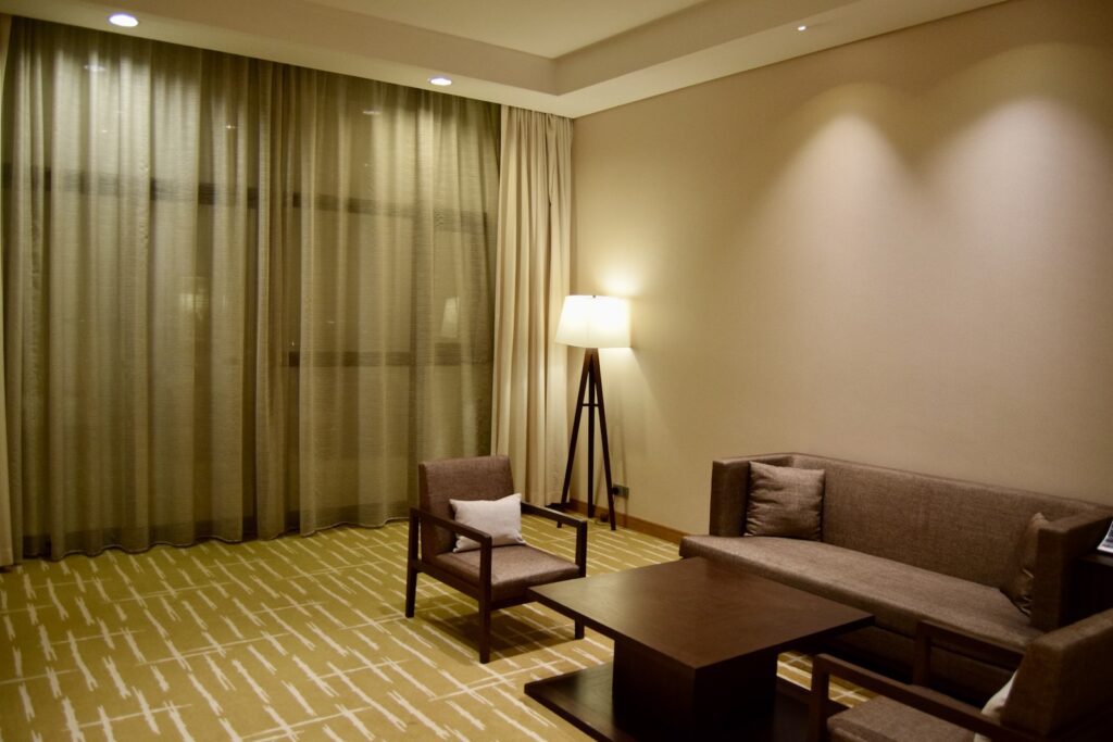Im Haus, Wand, Inneneinrichtung, Boden, Fensterausstattung, Tisch, Fußboden, Fensterabdeckung, Couch, Vorhang, Kaffeetisch, Bettsofa, Kleines Sofa, Tapete, Armlehne, Decke, Wohnzimmer, Lampenschirm, Bett, Stuhl, Zimmer, Hotel, Mobiliar
