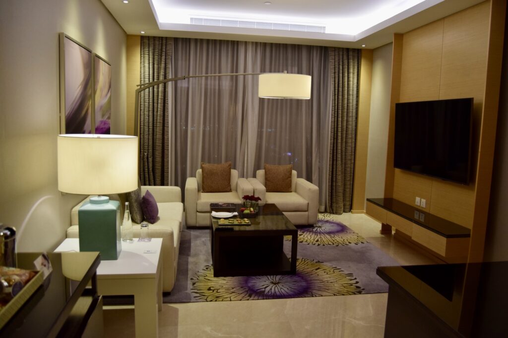 Im Haus, Inneneinrichtung, Wand, Tisch, Couch, Hotel, Vorhang, Kaffeetisch, Studiocouch, Bettsofa, Vase, Kissen, Boden, Kleines Sofa, Fensterausstattung, Stuhl, Bude, Zimmer, Decke, Fenster, Wohnzimmer, Fernsehen, Mobiliar